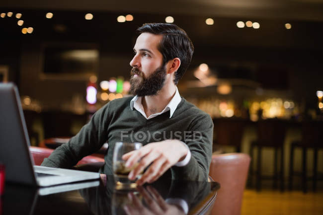 Uomo con bicchiere di bevanda e computer portatile sul tavolo nel bar — Foto stock