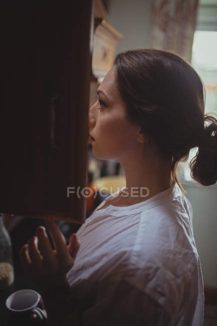 Donna che guarda nell'armadio della cucina a casa — Foto stock
