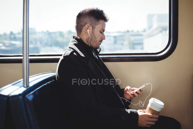 Бізнесмен тримає одноразову чашку кави і слухає музику на мобільному телефоні в поїзді — стокове фото