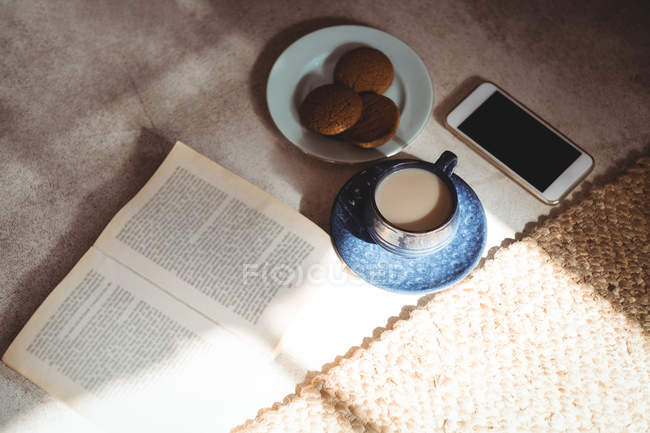 Livro, chá, biscoitos e telefone celular no chão em casa — Fotografia de Stock