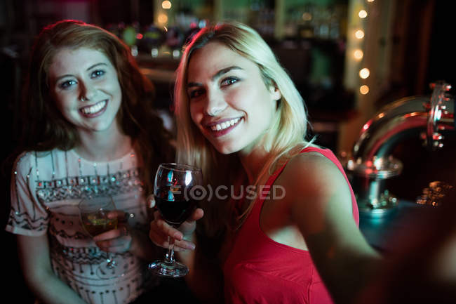 Amigos tomando selfie desde el teléfono móvil mientras toman vino en el mostrador en el bar - foto de stock