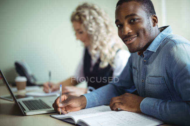 Retrato de ejecutivos de negocios tomando notas mientras utilizan el ordenador portátil en la oficina - foto de stock