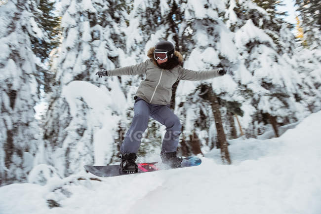 Жінка сноубордистка стрибає над схилом на снігу покритій горі — стокове фото