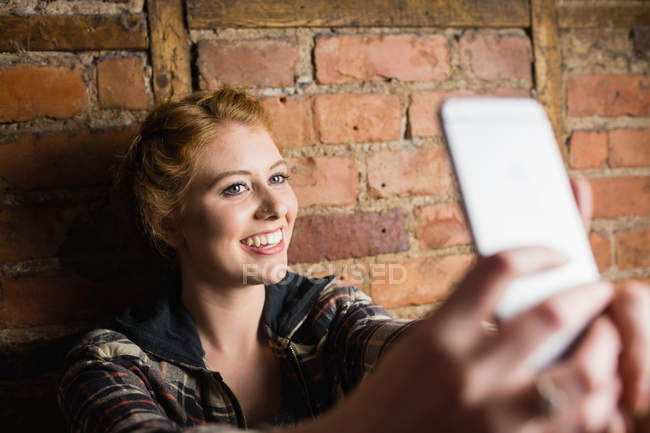 Жінка стоїть на цегляній стіні і бере селфі на свій мобільний телефон — стокове фото