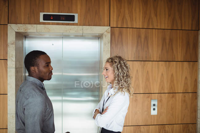 Executivos de negócios interagindo perto de elevador no escritório — Fotografia de Stock