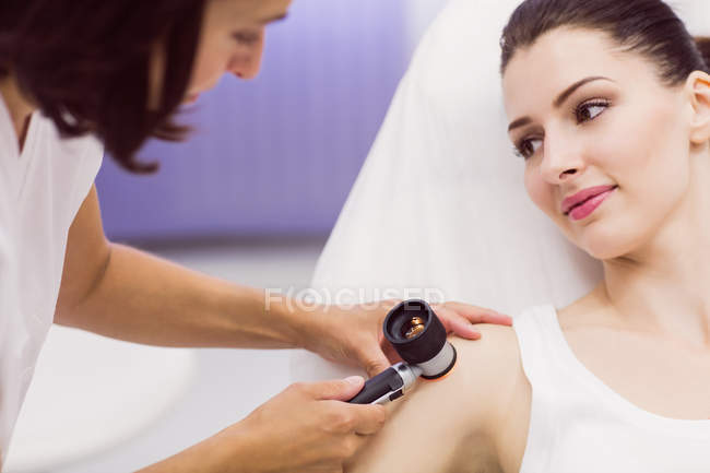 Dermatólogo examinando la piel del paciente con dermatoscopio en la clínica - foto de stock