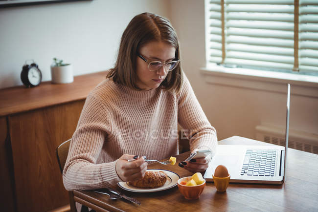 Frau benutzt Handy beim Frühstück im heimischen Wohnzimmer — Stockfoto
