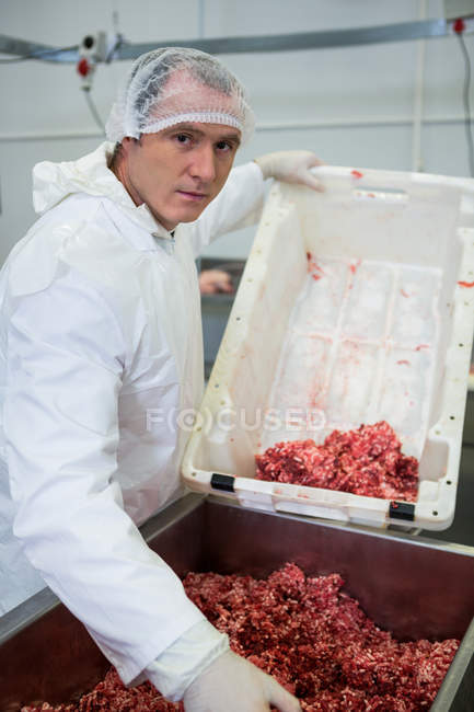 Retrato del carnicero vaciando carne picada en la máquina picadora de carne en la fábrica de carne - foto de stock