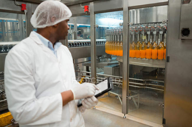 Работник мужского пола держит цифровой планшет во время проверки бутылки сока на заводе — стоковое фото