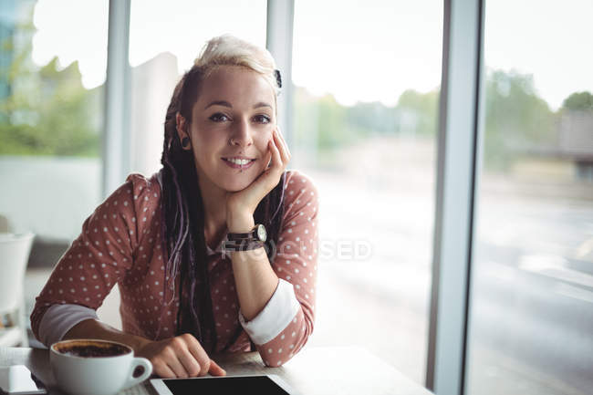 Retrato de mujer sonriente con taza de café y tableta digital en la mesa en la cafetería - foto de stock