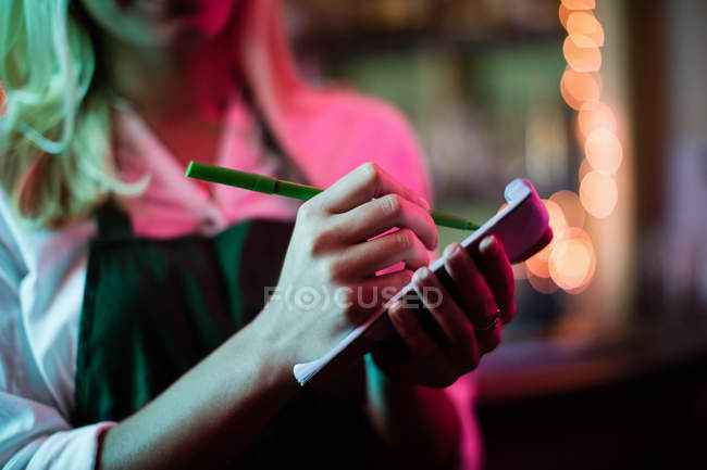 Meados de seção de garçonete escrevendo uma ordem no bloco de notas no bar — Fotografia de Stock