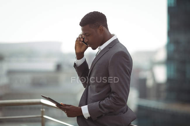 Бизнесмен, использующий цифровой планшет и разговаривающий по мобильному телефону на офисной террасе — стоковое фото