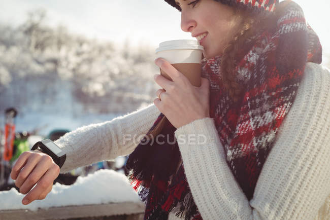 Жінка лижник дивиться її смарт-годинник, маючи каву на гірськолижному курорті — стокове фото