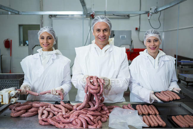 Retrato de carniceros empacando salchichas en fábrica de carne - foto de stock