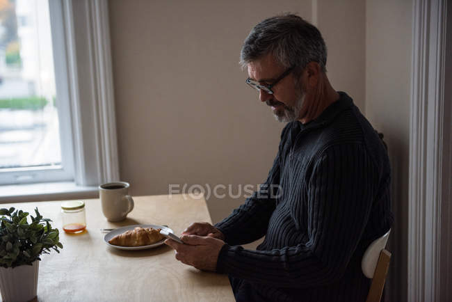 Uomo che utilizza il telefono cellulare mentre in soggiorno a casa — Foto stock