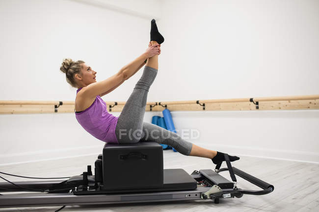 Mulher esticando as pernas no reformador no ginásio — Fotografia de Stock