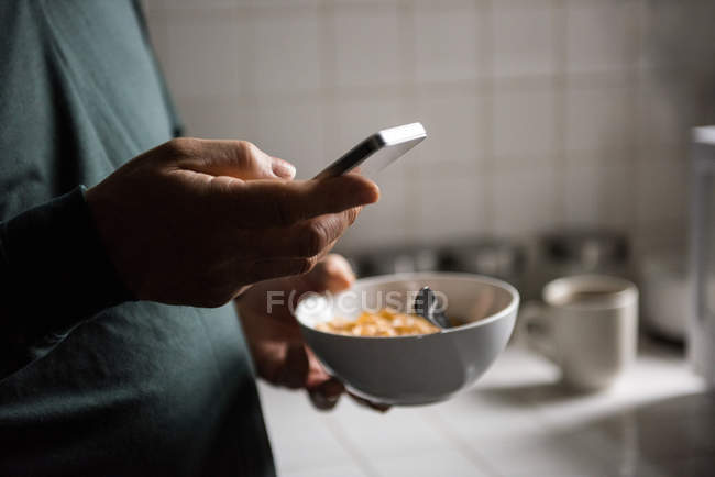 Средняя часть человека с помощью мобильного телефона во время завтрака на кухне дома — стоковое фото
