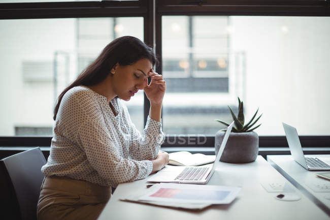 Напружена бізнес-леді сидить за своїм столом в офісі — стокове фото