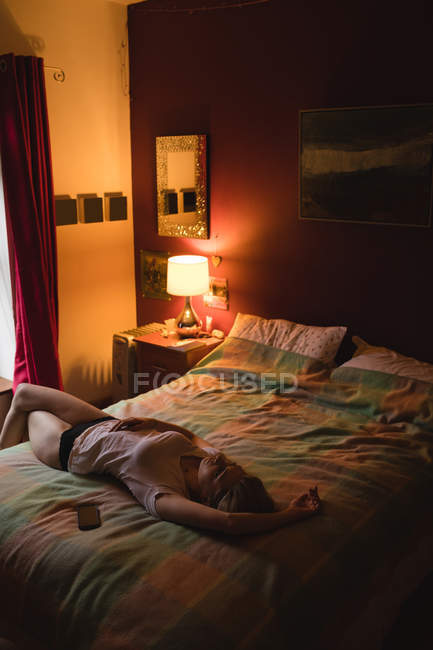 Mujer acostada en la cama en el dormitorio - foto de stock