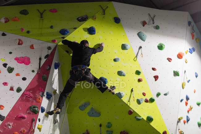 Hombre practicando escalada en roca en muro de escalada artificial en gimnasio - foto de stock