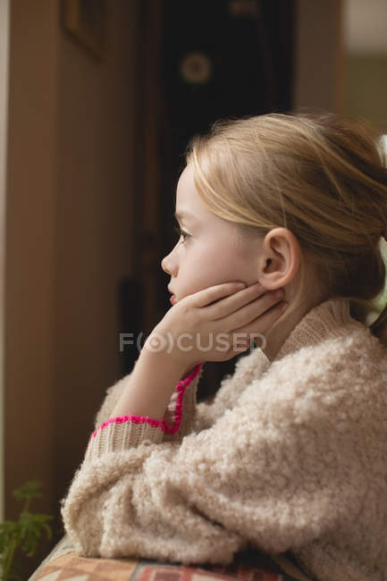 Thoughtful girl sitting on sofa in living room at home — Stock Photo