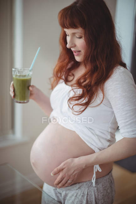 Femme enceinte réfléchie tenant un verre de jus à la maison — Photo de stock