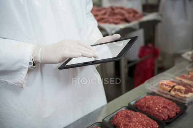 Section médiane du boucher tenant des dossiers sur tablette numérique à l'usine de viande — Photo de stock