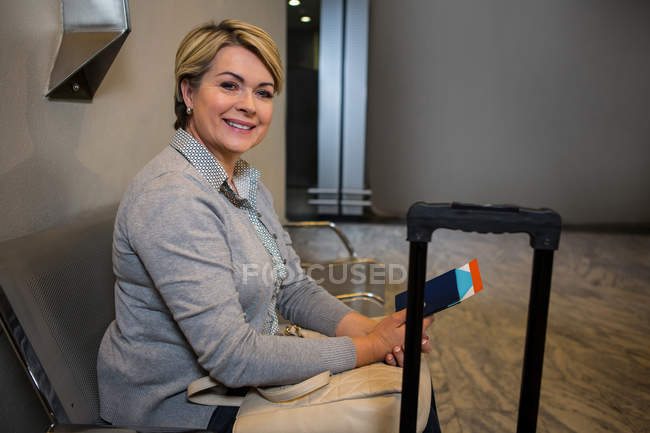 Businesswoman sitting with luggage and passport in waiting area in airport — Stock Photo