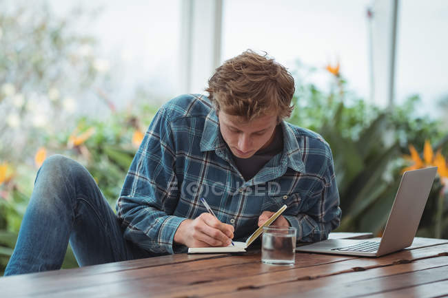 Мужчина сидит за столом и пишет заметки дома — стоковое фото
