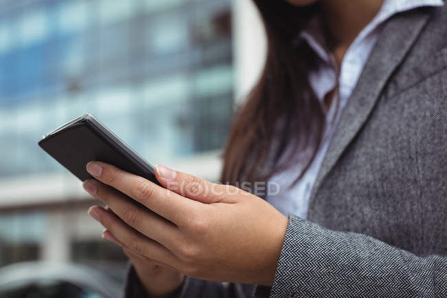 Mid-section of businesswoman text messaging on mobile phone while standing at city street — Stock Photo