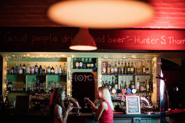 Mulheres interagindo enquanto tomam um copo de vinho no balcão no bar — Fotografia de Stock