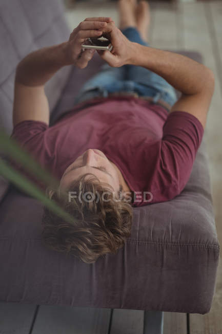 Чоловік лежить на дивані і використовує мобільний телефон у вітальні — стокове фото