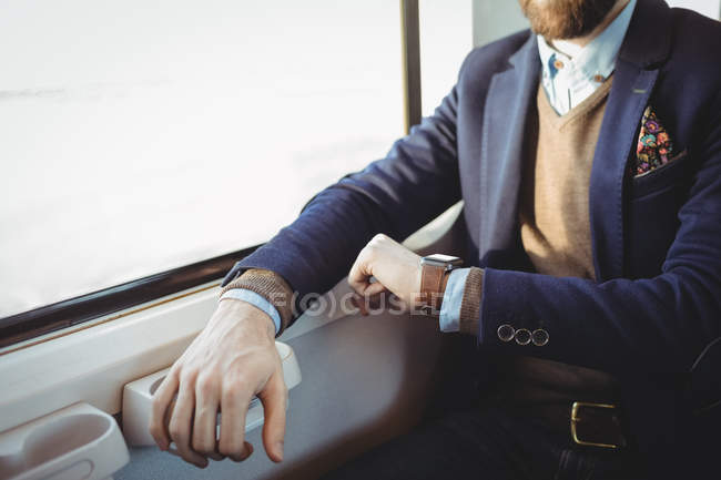 Mid-section of businessman checking time on smartwatch while travelling in train — Stock Photo