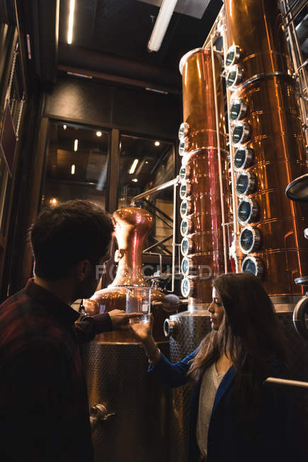 Homme et femme examinant un échantillon d'alcool dans une usine de bière — Photo de stock