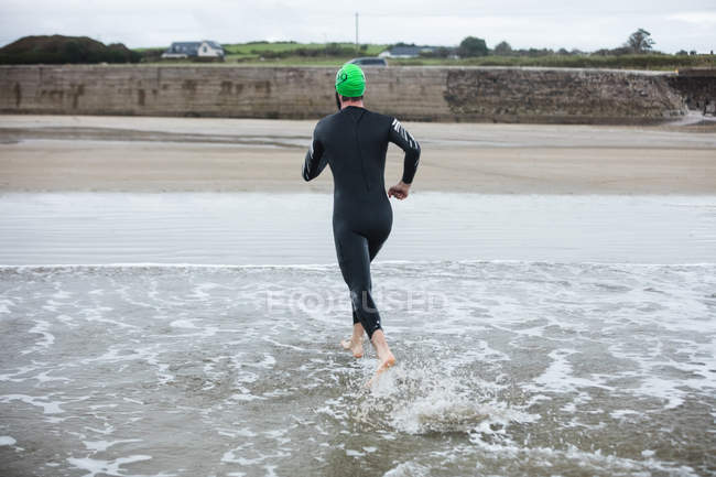 Вид сзади спортсмена, бегущего к пляжу — стоковое фото
