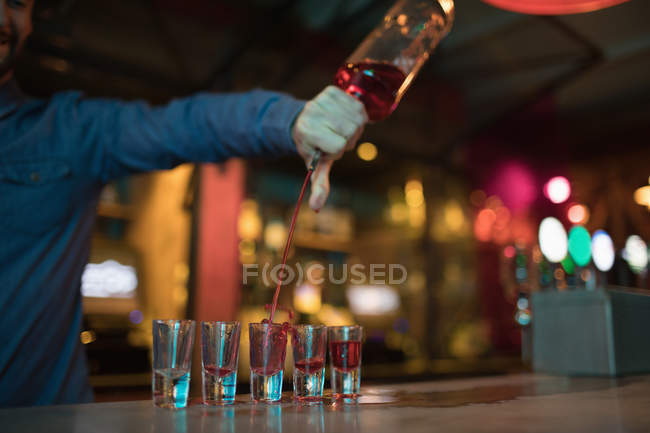 Bartender pouring alcoholic drink in shot glasses at bar — Stock Photo