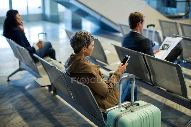Cercanías con taza de café usando teléfono móvil en la sala de espera en el aeropuerto - foto de stock