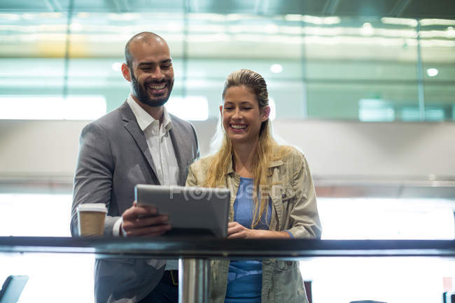 Pareja sonriente usando tableta digital en la sala de espera en la terminal del aeropuerto - foto de stock