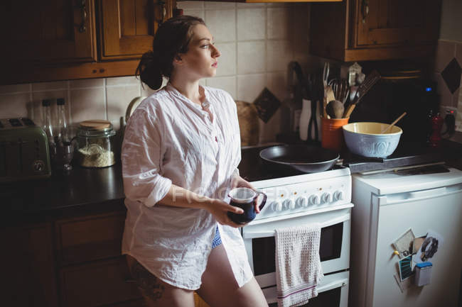 Mujer reflexiva sosteniendo la taza de café en la cocina en casa - foto de stock