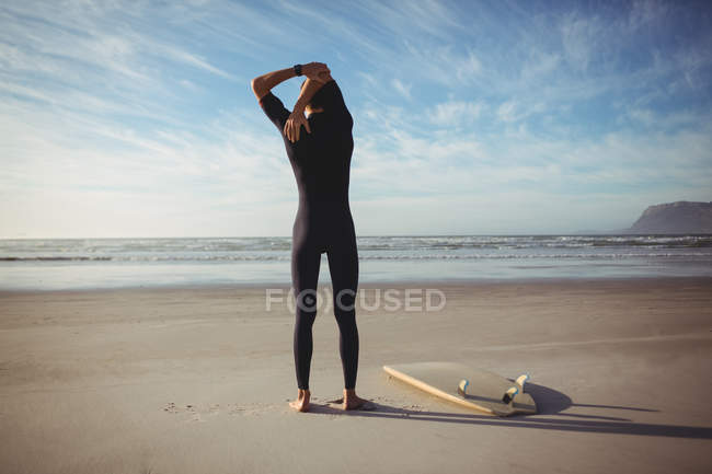 Rear view of man with surfboard exercising on beach — Stock Photo