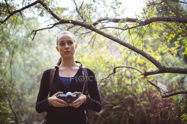 Mulher bonita de pé com câmera na floresta — Fotografia de Stock