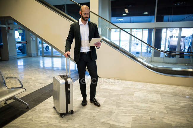 Businessman standing with luggage using digital tablet in waiting area at airport terminal — Stock Photo