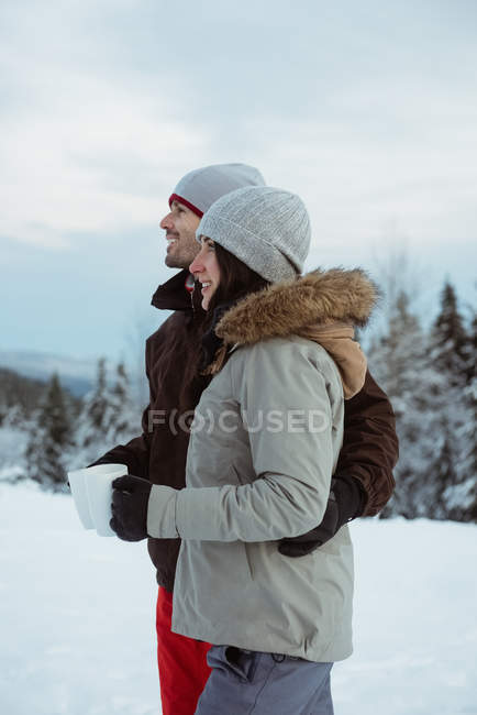 Feliz pareja de pie y sosteniendo la taza en la montaña cubierta de nieve - foto de stock