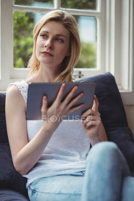 Задумчивая женщина, использующая цифровой планшет в гостиной дома — стоковое фото