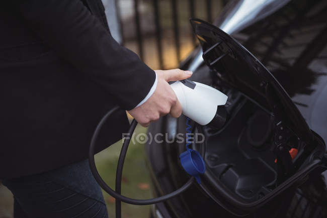 Partie médiane de la femme rechargeant la voiture électrique à la station de recharge du véhicule — Photo de stock