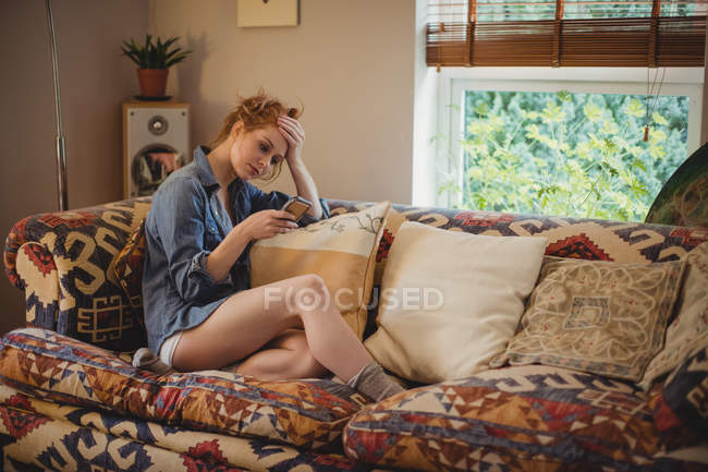 Напружена жінка використовує мобільний телефон у вітальні вдома — стокове фото