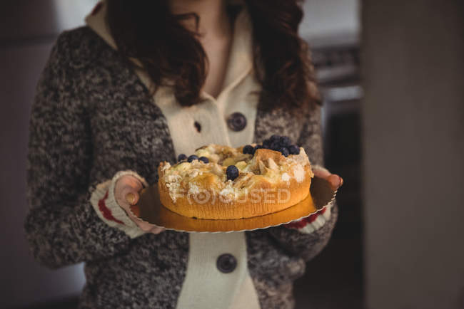 Mid section of woman holding blueberry cake in living room at home — Stock Photo