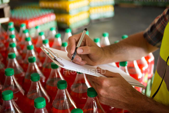 Mid section of male worker noting about products in juice factory — Stock Photo