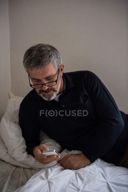 Uomo che utilizza il telefono cellulare sul letto a casa — Foto stock