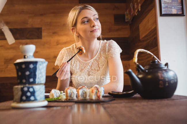 Задумчивая женщина ест суши в ресторане — стоковое фото